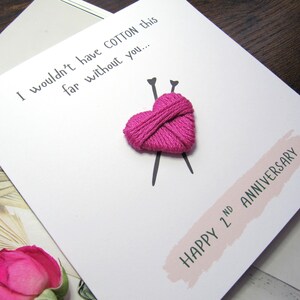 May include: White card featuring a pink embroidered heart and knitting needles. The text reads "I wouldn't have COTTON this far without you..." and "HAPPY 2nd ANNIVERSARY" on a pink banner. A pink rose is visible.