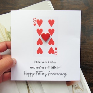 May include: A white square card with a playing card design showing nine red hearts and the number six. The text says "Nine years later and we're still kiln it! Happy Pottery Anniversary."