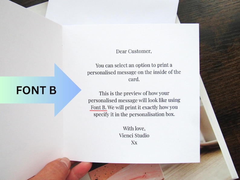 May include: An open greeting card with text. The card's interior displays a message about personalised printing using Font B. A blue and green arrow points to the text "FONT B". The card is held open, revealing the printed message.