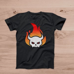 May include: Black t-shirt featuring a white skull with red eyes and horns, set against a fiery orange and red flame design. The graphic is centered on the front of the shirt, creating a bold and eye-catching look. The shirt is made of a soft material.