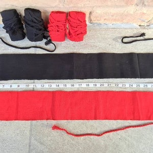 May include: A flat lay of black and red martial arts equipment. Two black and two red hand wraps are at the top. Below are two belts, one black and one red, with a measuring tape alongside.