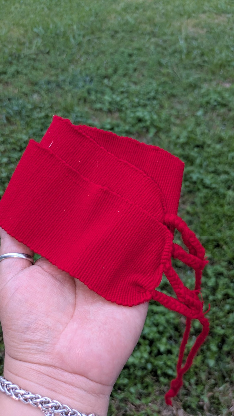 May include: Bright red fabric wristbands with braided ties. The wristbands are made of a ribbed material and are folded over. The background is green grass.