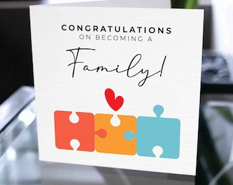 May include: Congratulations on becoming a family card with a red heart and three puzzle pieces in orange, red, and blue.