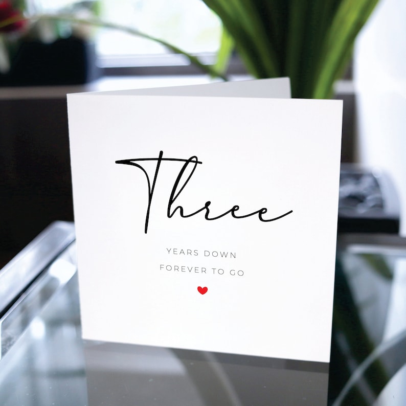 May include: A white card with black text that reads "Three Years Down Forever To Go" with a small red heart below the text.