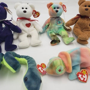 May include: A collection of six colorful beanie baby toys, including a purple bear, a white bear, a tie-dye bear, a brown bear, a green and blue snake, and a multi-colored chameleon.
