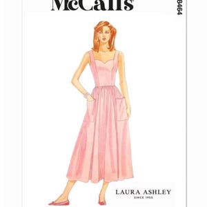 May include: A McCall's sewing pattern featuring a pink dress design. The illustration shows a sleeveless dress with a sweetheart neckline, pockets, and a flared skirt. The Laura Ashley logo is visible.