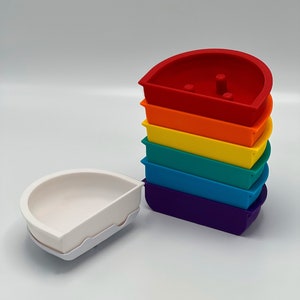 May include: A set of seven nesting bowls in rainbow colours. The bowls are made of plastic and are shaped like half-circles. The bowls are stacked on top of each other, with the largest bowl at the bottom and the smallest bowl at the top. The bowls are all different colours, starting with red at the bottom and ending with purple at the top.