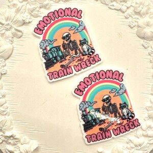 May include: Two stickers with a skeleton and a train on a white background. The stickers say "Emotional Train Wreck" with a rainbow and clouds.