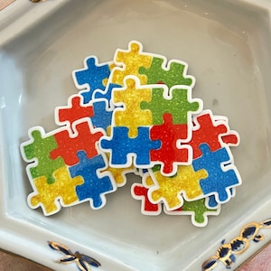 May include: A white ceramic hexagonal dish with a gold rim and blue dragonfly designs. The dish contains a pile of colorful puzzle pieces with glitter.