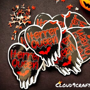 May include: A set of black and red heart-shaped stickers with the text "Horror Queen" and a bat graphic. The stickers have a dripping effect and are perfect for Halloween.