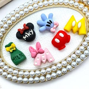 May include: An oval, pearl-bordered tray with various colorful cartoon-themed embellishments. The tray features a gold frame and is adorned with small, decorative items including a black bow with "mky" text, blue gloves, red gloves, and yellow gloves.