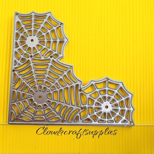 May include: A silver-colored metal die cut in the shape of a spider web, with a corner design. The die cut is on a yellow background. The text "Cloudcraftsupplies" is written in black script at the bottom.