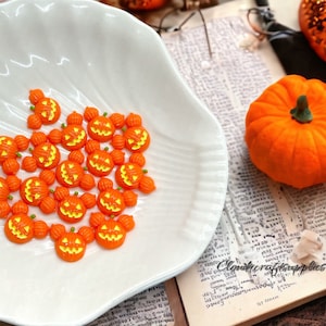 May include: A white ceramic plate filled with orange and yellow Halloween pumpkin shaped embellishments.