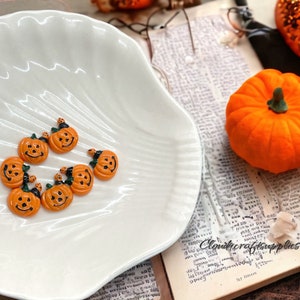 May include: A white ceramic dish with eight small orange pumpkin-shaped decorations. The pumpkins have black painted faces and green stems.