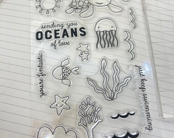 May include: Clear stamp sheet with ocean-themed illustrations, including a turtle, jellyfish, seaweed, starfish, sun, waves, and the text "sending you oceans of love" and "you're fantastic" and "just keep swimming".