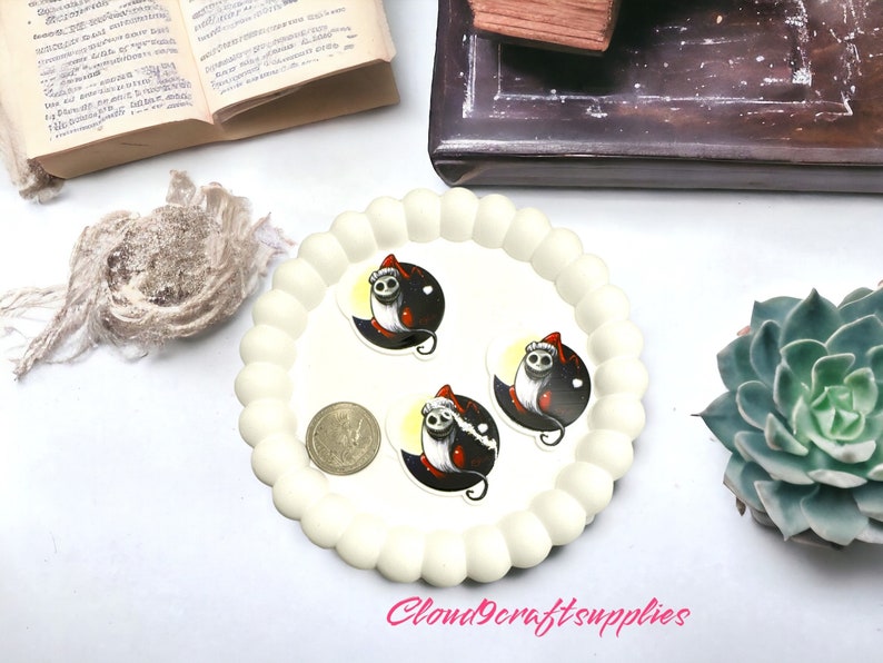 May include: A cream-coloured, scalloped-edge tray holds three stickers featuring a cartoon character in a Santa hat against a black and yellow background. A coin and a succulent plant are also visible. The text "Cloud9craftsupplies" is in the bottom right corner.