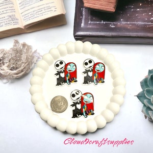May include: A white, scalloped-edge tray holds three small, colourful stickers featuring Jack Skellington and Sally from The Nightmare Before Christmas. A coin is also on the tray. The text "Cloud9craftsupplies" is visible.
