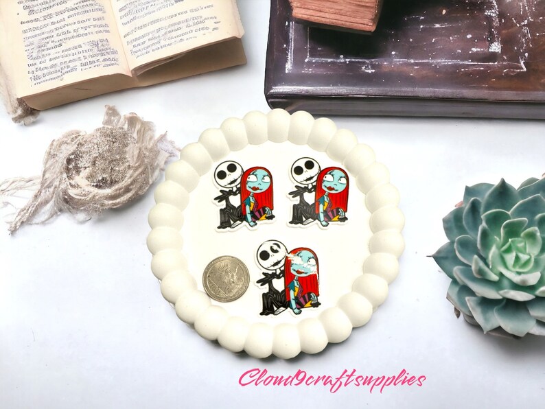 May include: A white, scalloped-edge tray holds three small, colourful stickers featuring Jack Skellington and Sally from The Nightmare Before Christmas. A coin is also on the tray. The text "Cloud9craftsupplies" is visible.