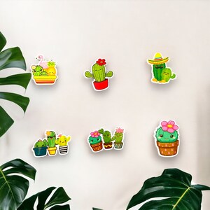 May include: A collection of six colorful cactus stickers with smiling faces and various accessories. The stickers feature different cactus designs, including one with a sombrero and another with a flamingo and pineapple. The stickers are on a white background.