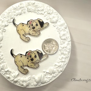 May include: Two white ceramic Dalmatian puppy figurines with black spots on a white background with a floral design. The figurines are approximately 2 inches tall.