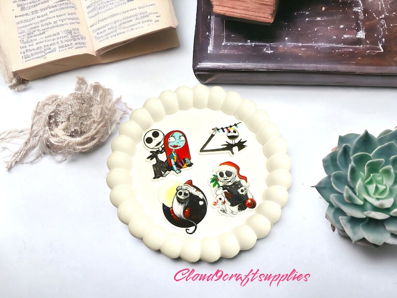 May include: A cream-coloured, scalloped-edge tray displays four character stickers from The Nightmare Before Christmas. The stickers feature Jack Skellington and Sally, Jack with Christmas lights, a Jack-O-Lantern, and Jack with a Santa hat. The text "Cloud9craftsupplies" is visible.