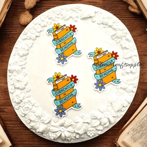 May include: Three yellow and orange book stack stickers with blue ribbon and floral accents. The stickers say "Currently Reading".