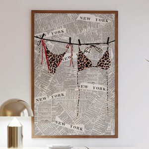 May include: A framed print of a leopard print bikini hanging on a clothesline against a background of a newspaper with the words "NEW YORK" repeated throughout.