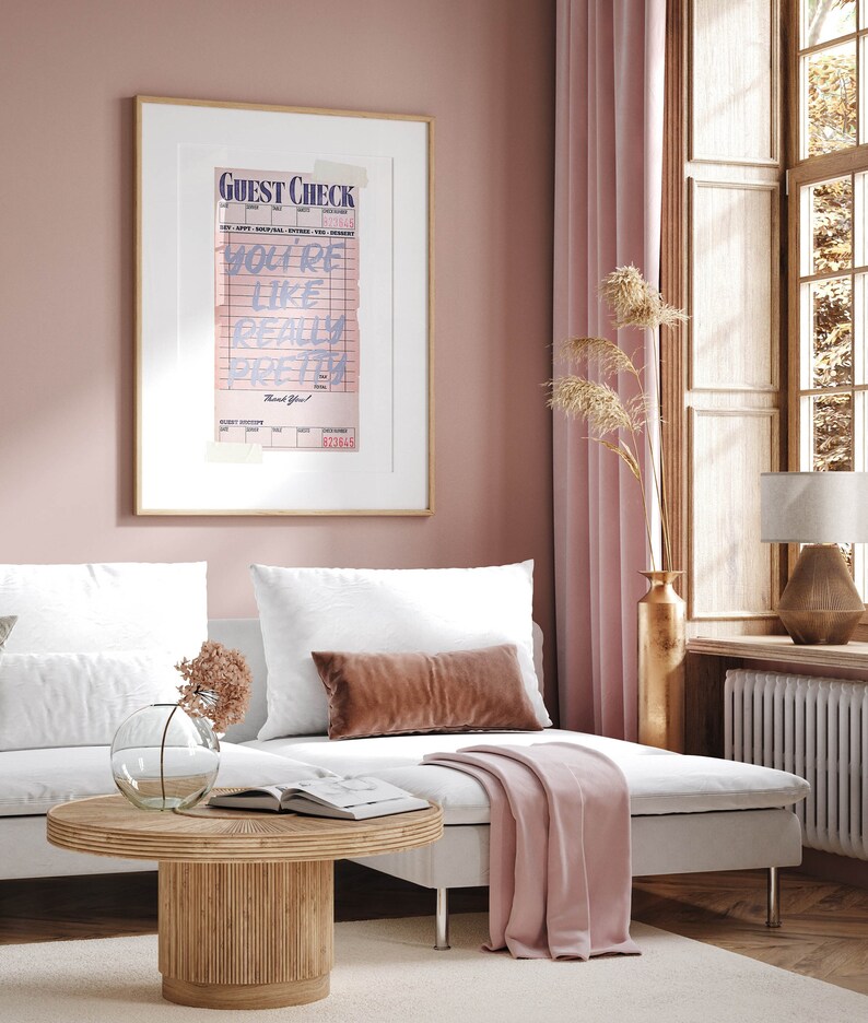 K&ouml;nnte beinhalten: Ein gerahmter Druck eines rosa und blauen Gastchecks mit dem Text "You're like really pretty" auf wei&szlig;em Hintergrund. Der Druck h&auml;ngt an einer hellrosa Wand &uuml;ber einem wei&szlig;en Sofa mit einer rosa Wolldecke.