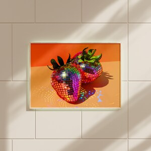 May include: Two iridescent disco ball strawberries on a peach background. The strawberries are made of small, mirrored tiles that reflect light in a rainbow of colors.