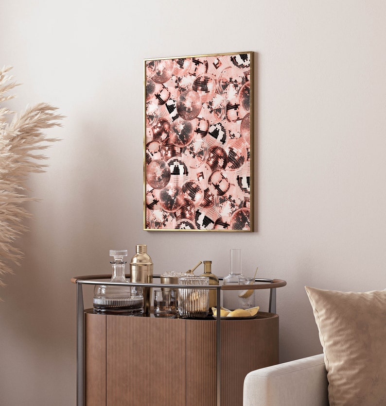 May include: A framed print of a pink and white disco ball pattern. The print is in a gold frame and is hanging on a white wall.