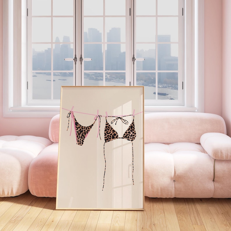 May include: A framed print of a leopard print bikini hanging on a clothesline. The bikini is pink and black with a white background.