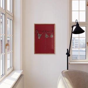 May include: A framed print of a leopard print bikini hanging on a clothesline against a red background.