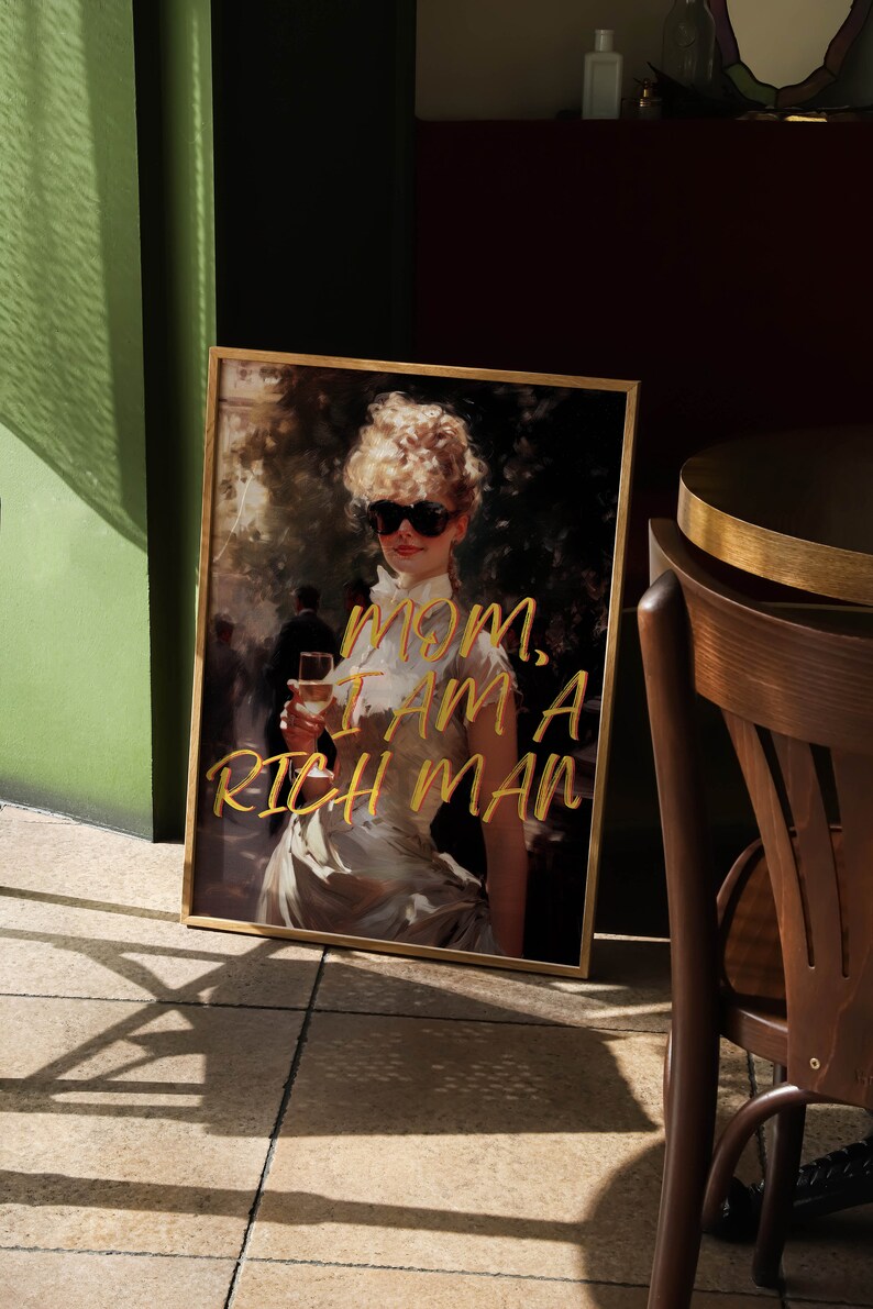 May include: A framed print of a woman wearing sunglasses and a white dress, holding a glass of wine. The text "MOM, I AM A RICH MAN" is written in gold lettering on the print.