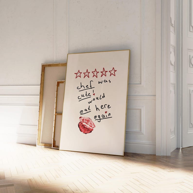 Op de afbeelding: Een witte poster met een gouden lijst met een vijfsterrenbeoordeling en de tekst "kok was schattig! zou hier weer eten" met een rode lippenstiftkus.