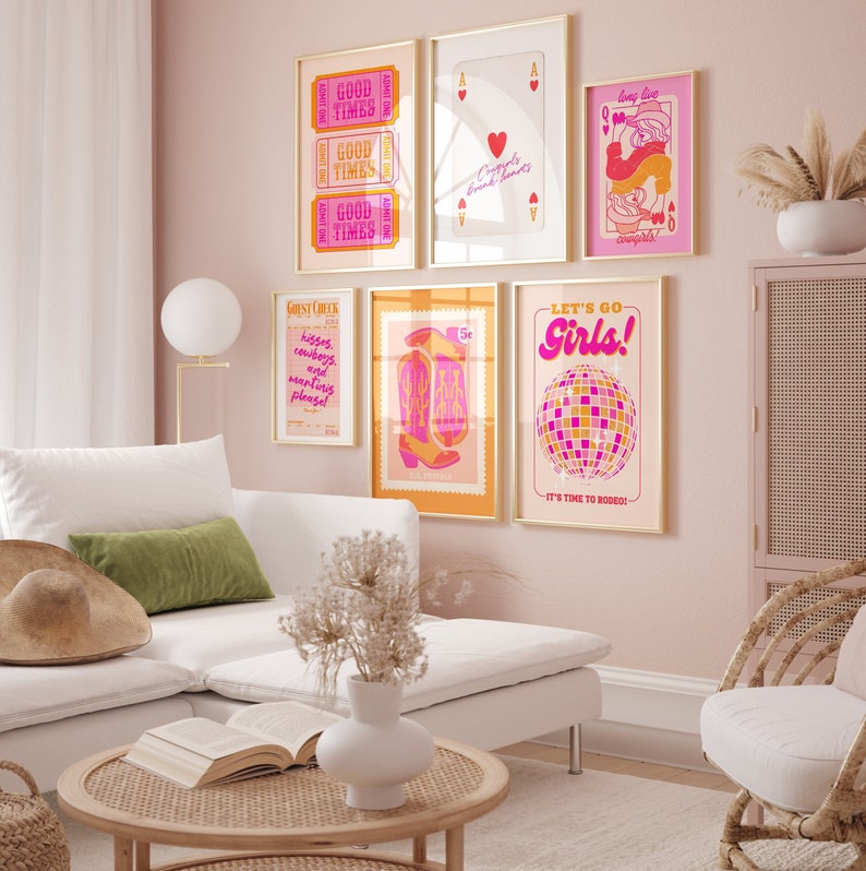 May include: A set of six framed prints with a pink and orange color scheme. The prints feature various designs, including a disco ball, cowboy boots, a playing card, and a ticket stub. The prints are hung on a pink wall in a living room setting.