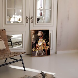 May include: A framed print of a woman in a white dress and sunglasses holding a glass of wine. The text "MOM, I AM A RICH MAN" is written in gold lettering on the print.