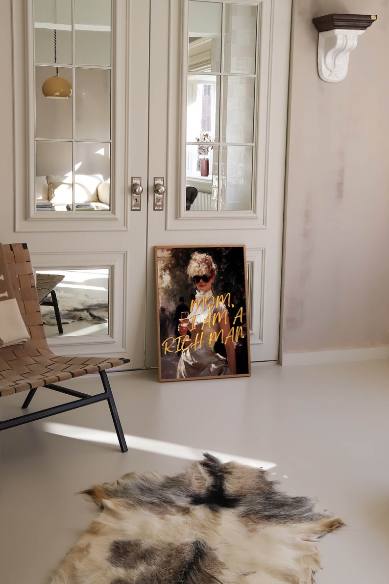 May include: A framed print of a woman in a white dress and sunglasses holding a glass of wine. The text "MOM, I AM A RICH MAN" is written in gold lettering on the print.