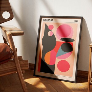 May include: A framed poster featuring a geometric design in black, red, orange, pink, and blue. The poster has the text "BAUHAUS 1923" at the top.