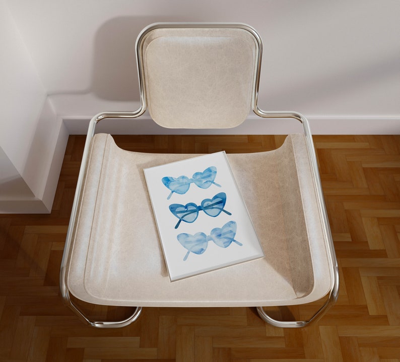 May include: A white chair with a chrome frame and a white cushion. A white card with a blue watercolor illustration of three pairs of sunglasses is on the cushion.