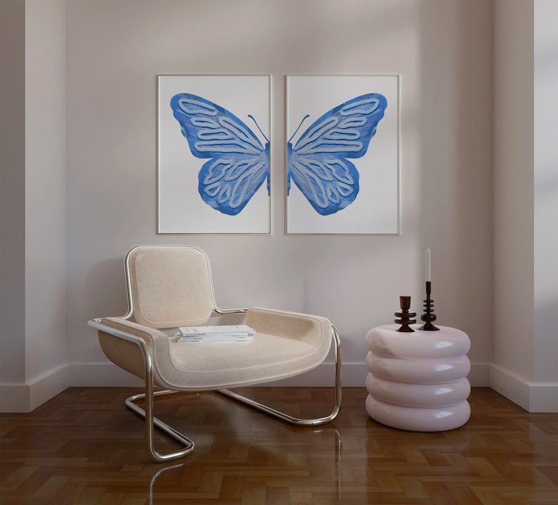 May include: A light beige armchair with a chrome frame sits in a room with a light pink side table and two candlesticks. Two framed prints of a blue butterfly are on the wall behind the chair.