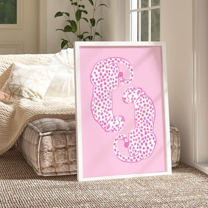 May include: A framed print featuring two pink cheetahs with black spots, curled up together on a pink background.