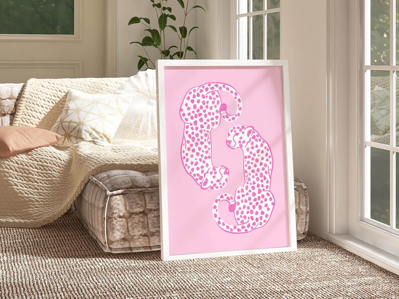 May include: A framed print featuring two pink cheetahs with black spots, curled up together on a pink background.