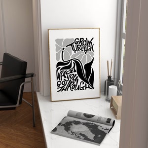 Puede incluir: Un p&oacute;ster en blanco y negro con un dise&ntilde;o floral y el texto "GROW THROUGH WHAT YOU GO THROUGH". El p&oacute;ster est&aacute; enmarcado en un marco dorado y est&aacute; colgado en una pared blanca.