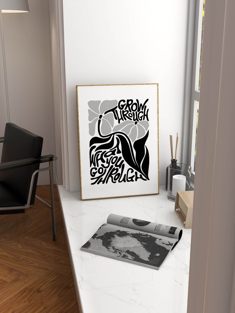 Puede incluir: Un p&oacute;ster en blanco y negro con un dise&ntilde;o floral y el texto "GROW THROUGH WHAT YOU GO THROUGH". El p&oacute;ster est&aacute; enmarcado en un marco dorado y est&aacute; colgado en una pared blanca.