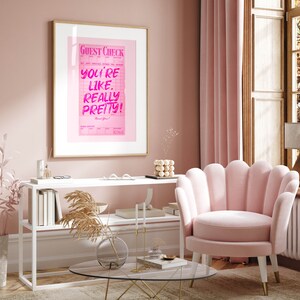 May include: A pink framed poster with the text "GUEST CHECK" and "YOU'RE LIKE, REALLY PRETTY!" in pink lettering on a pink background.