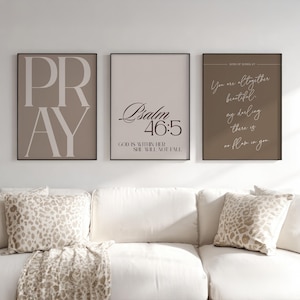 Puede incluir: Tres impresiones enmarcadas con citas inspiradoras. La primera impresión dice "PRAY" en letras blancas grandes sobre un fondo topo. La segunda impresión dice "Salmo 46:5" sobre un fondo beige claro. La tercera impresión tiene un fondo marrón con una cita.