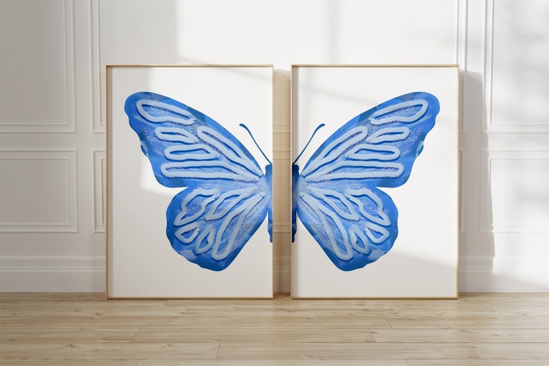 May include: Two framed prints of a blue butterfly with white details. The butterfly is depicted with its wings spread wide, creating a symmetrical design.