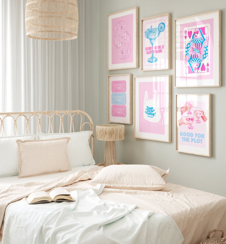 Puede incluir: Un dormitorio con una colcha rosa claro y una cabecera de mimbre. La pared es verde claro y tiene varias impresiones enmarcadas con ilustraciones rosas y azules. Las impresiones incluyen una copa de c&oacute;ctel, una carta de juego y una bolsa de la compra con el texto "&iexcl;Gracias por venir!" Las impresiones tambi&eacute;n incluyen el texto "Good Times" y "Good for the Plot".