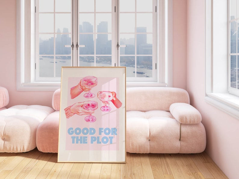 May include: A framed pink and blue poster with an illustration of three hands holding champagne flutes. The text "GOOD FOR THE PLOT" is printed in blue letters.