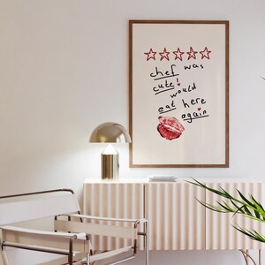 Op de afbeelding: Een ingelijst print met een vijfsterrenbeoordeling en de tekst "kok was schattig! zou hier weer eten" met een rode lippenstiftkus.